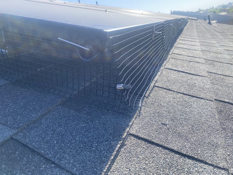 Close-up of critter-guard mesh and fasteners sealing the gap beneath solar panels